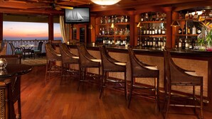 Zona de bar con mobiliario de madera, una pantalla de televisión y estantes llenos de botellas de licores.