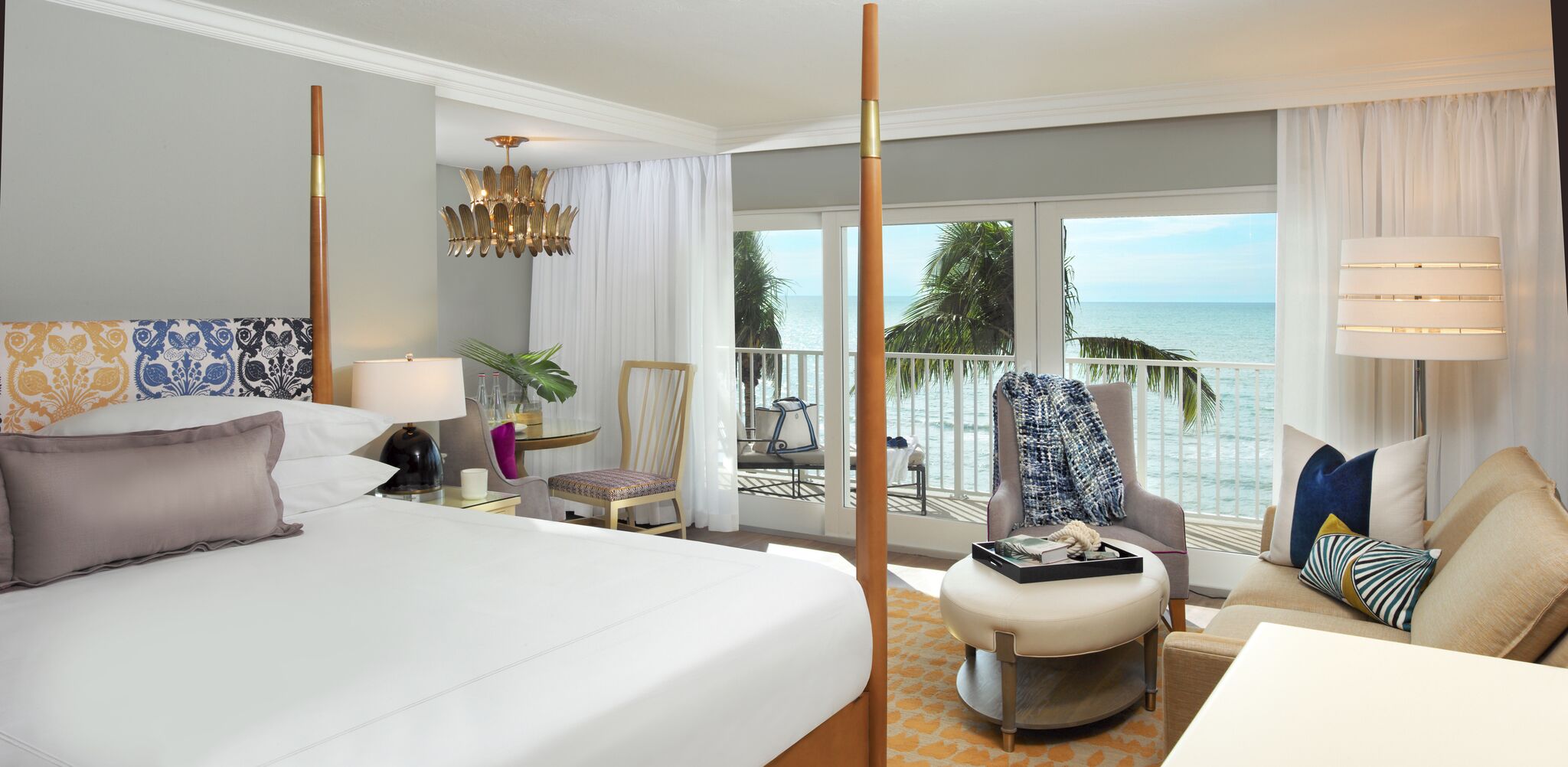 Une chambre d’hôtel avec un grand lit, une chaise, une petite table, une lampe et une vue sur l’océan.