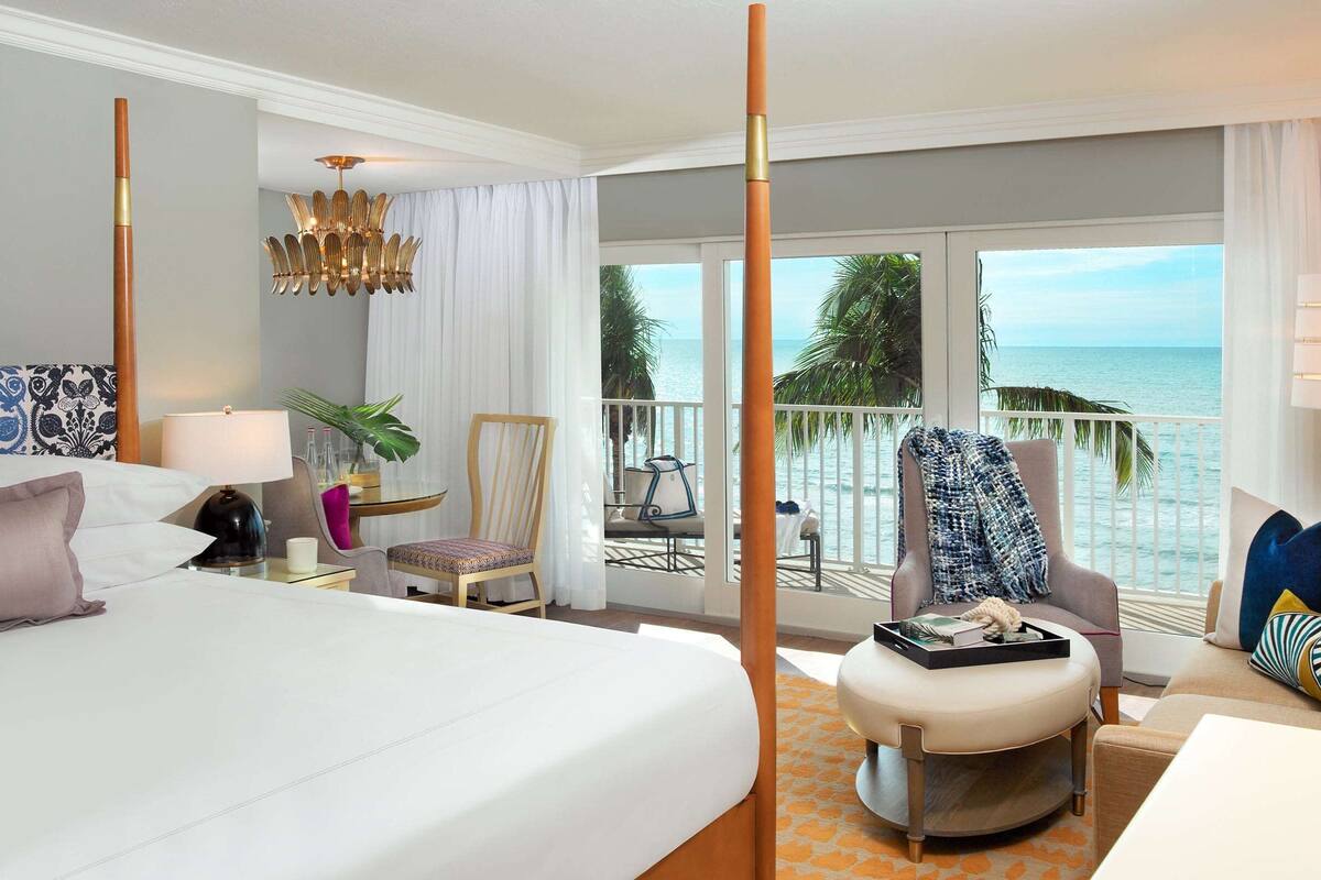 Une chambre d’hôtel dotée d’un grand lit, d’un coin salon avec vue sur l’océan et d’un balcon avec une chaise et une table.