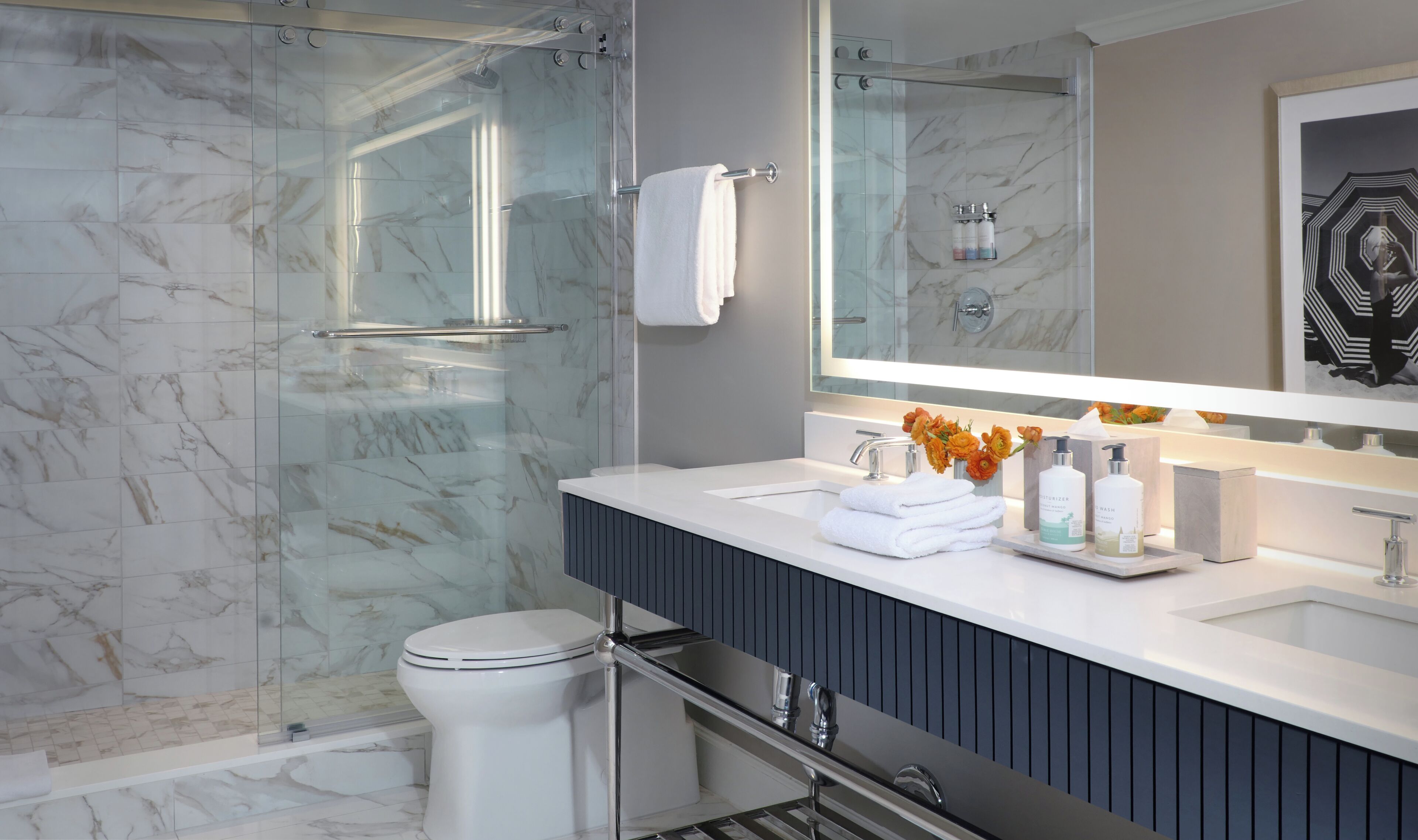 Un baño moderno con cabina de ducha de vidrio, inodoro blanco, tocador con espejo y artículos de aseo.