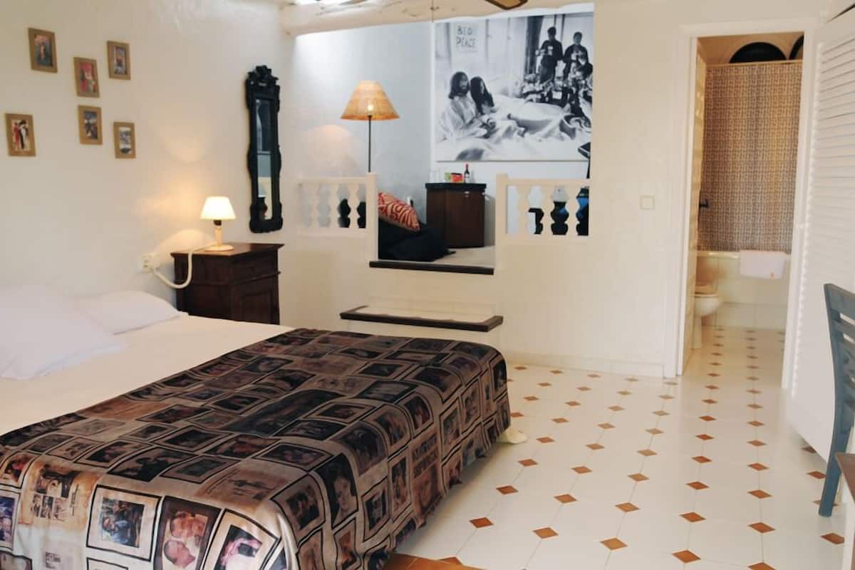 Un dormitorio con cama, mesita de noche, lámpara, cómoda, espejo y una pared con cuadros.