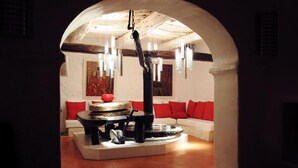 Un saló d'estar acollidor amb una taula circular al centre, un sofà amb coixins vermells i una làmpada penjant.