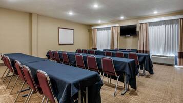 Un salón de conferencias con una larga mesa, sillas rojas, una pantalla de proyector y un televisor en la pared.