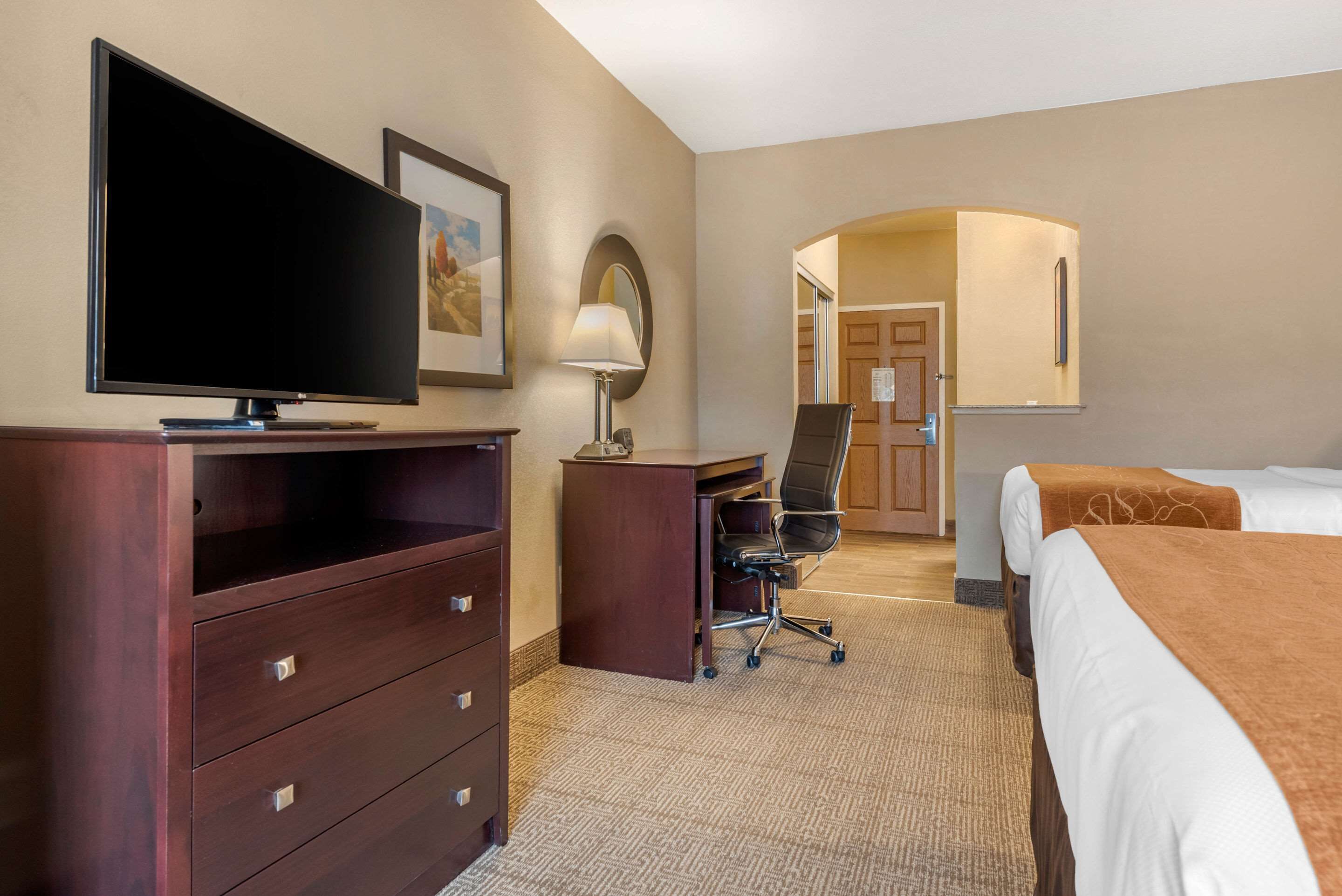 A hotel room with a TV, desk, chair, and two beds.