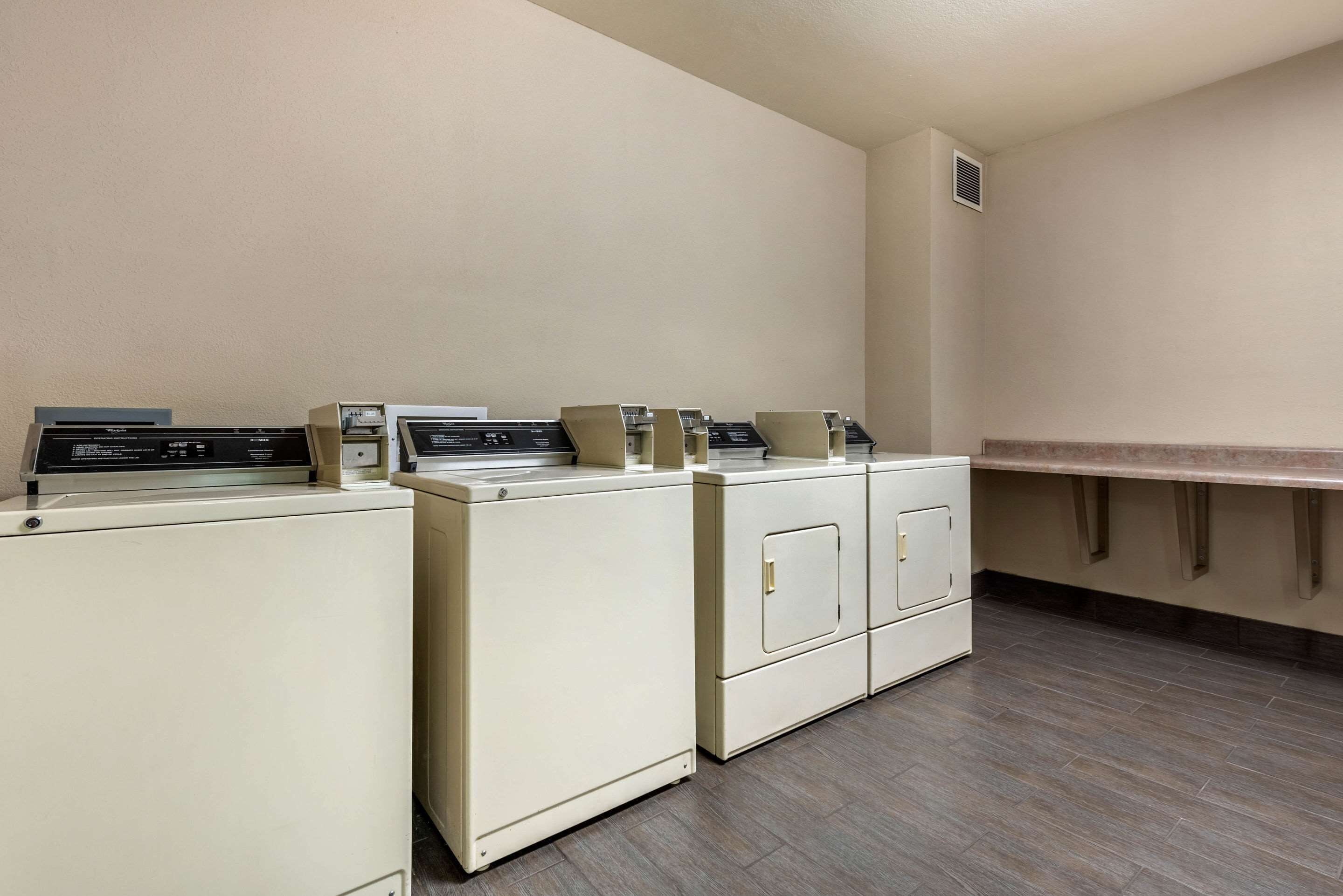 A laundry area with four washers and dryers, a countertop, and a vent on the wall.