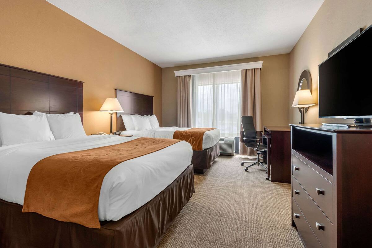 Ein Hotelzimmer mit zwei Betten, einem Schreibtisch, einem Fernseher und einem fenster mit Vorhängen.