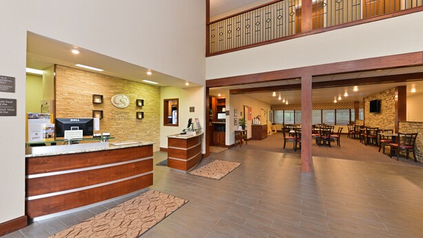 A hotel lobby with a reception desk, a clock, and a seating area with tables and chairs.
