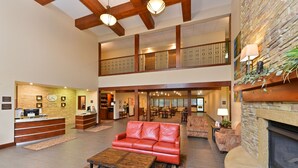 A spacious lobby with a reception desk, leather seating, a fireplace, and a second-floor balcony.