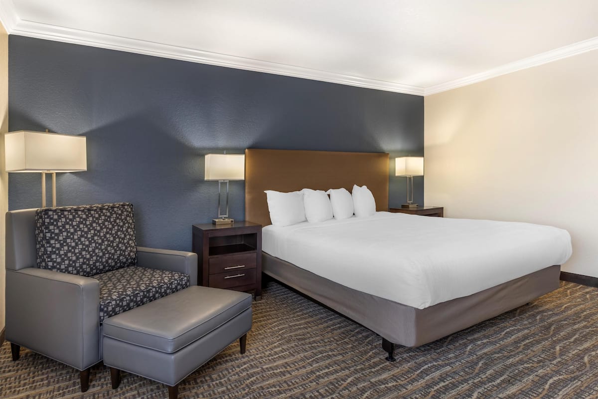A hotel room with a large bed, two bedside tables with lamps, a patterned armchair, and a footstool.