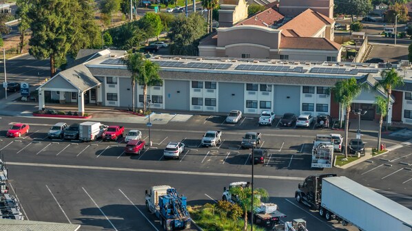 An aerial view of a hotel with a parking lot, multiple vehicles, and surrounding buildings.