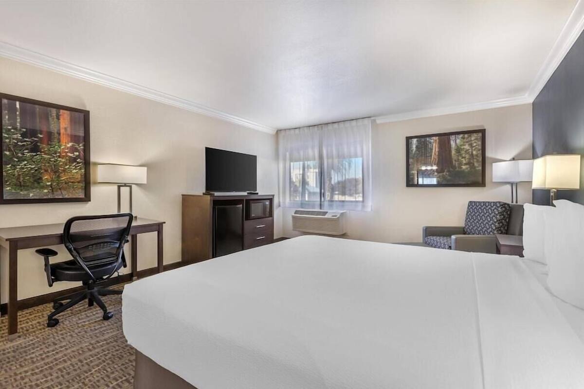 A hotel room with a large bed, a desk with a chair, a television, and two paintings on the walls.