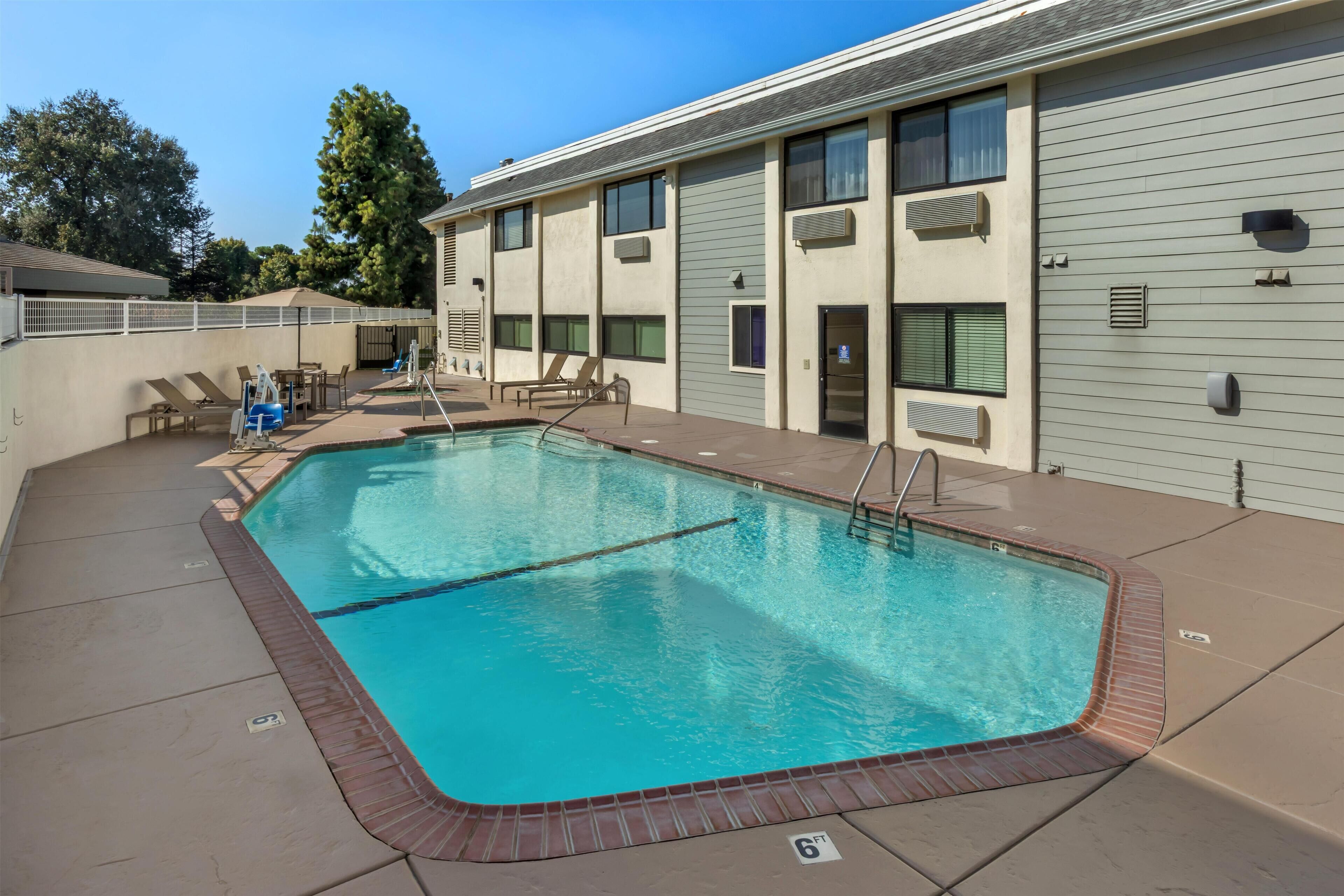 A swimming pool with a brick border, lounge chairs, and a covered seating area.