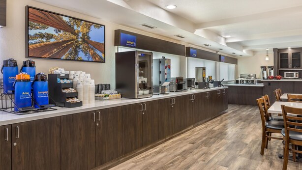 A modern hotel kitchen with a long counter, coffee machines, and a large painting of a tree. - Best Western Town & Country Lodge (Tulare)