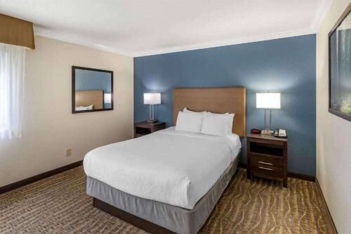 A hotel room with a bed, two bedside tables, a nightstand, and a large mirror.