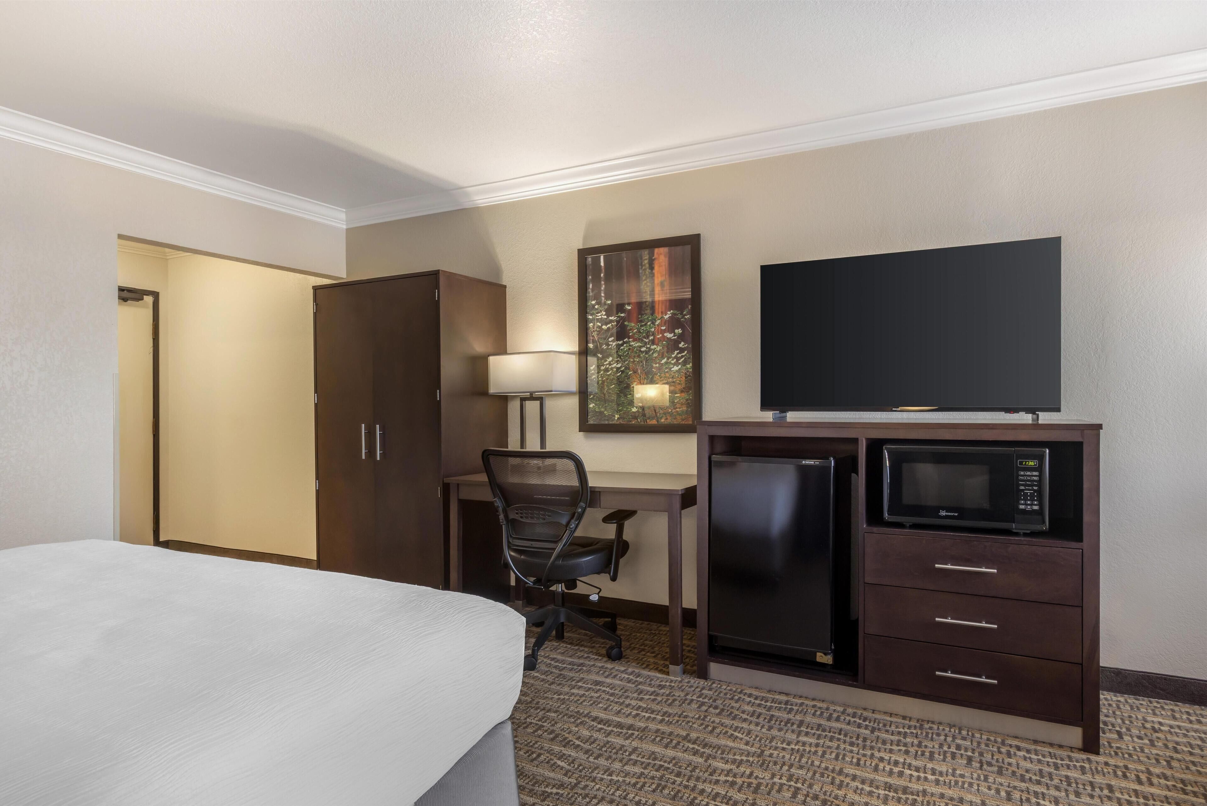 Una habitación de hotel con cama, escritorio, silla, televisor y minibar.
