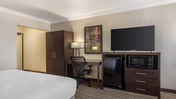 A hotel room with a bed, desk, chair, television, and a minibar.