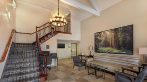 A spacious lobby with a grand staircase, a large forest-themed painting, and a comfortable seating area. - Best Western Town & Country Lodge (Tulare)