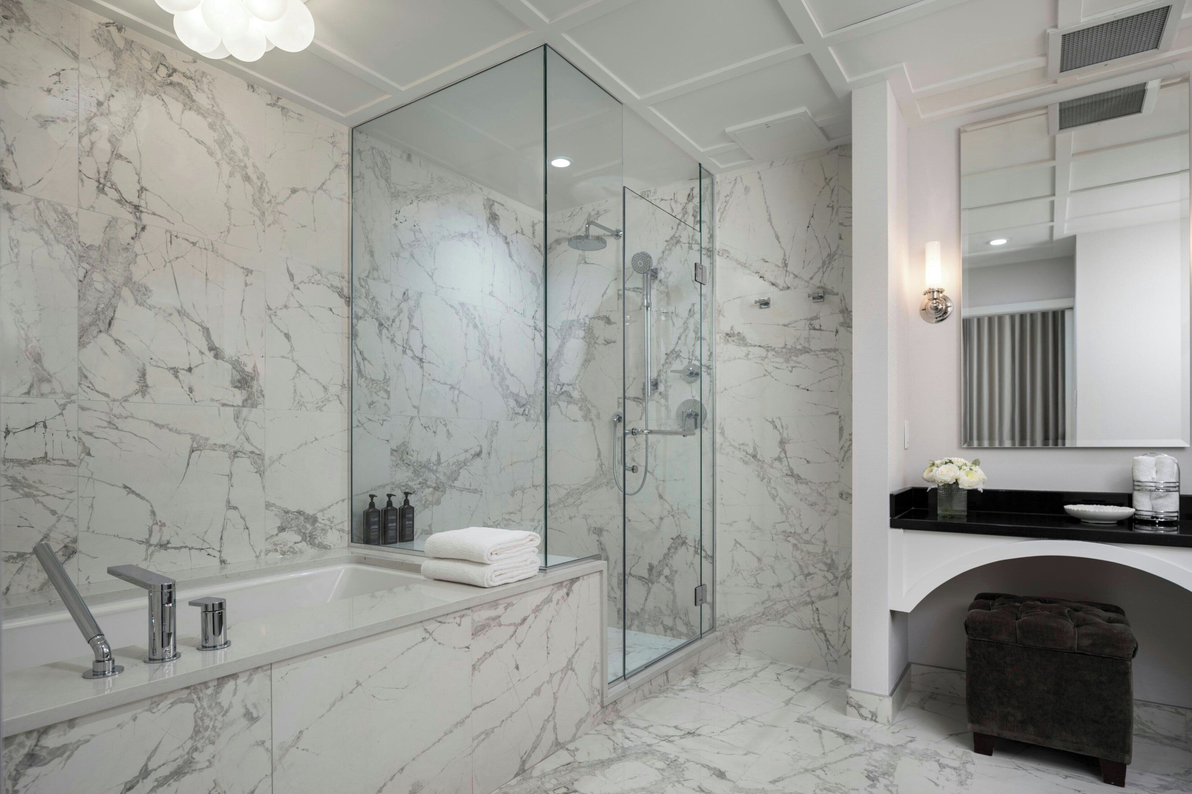 A modern bathroom with a glass-enclosed shower, a marble-tiled floor, and a black countertop with a sink and mirror.