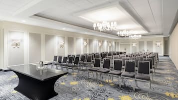 Une salle de conférence avec une longue table, des rangées de chaises, des lustres et une moquette à motifs.