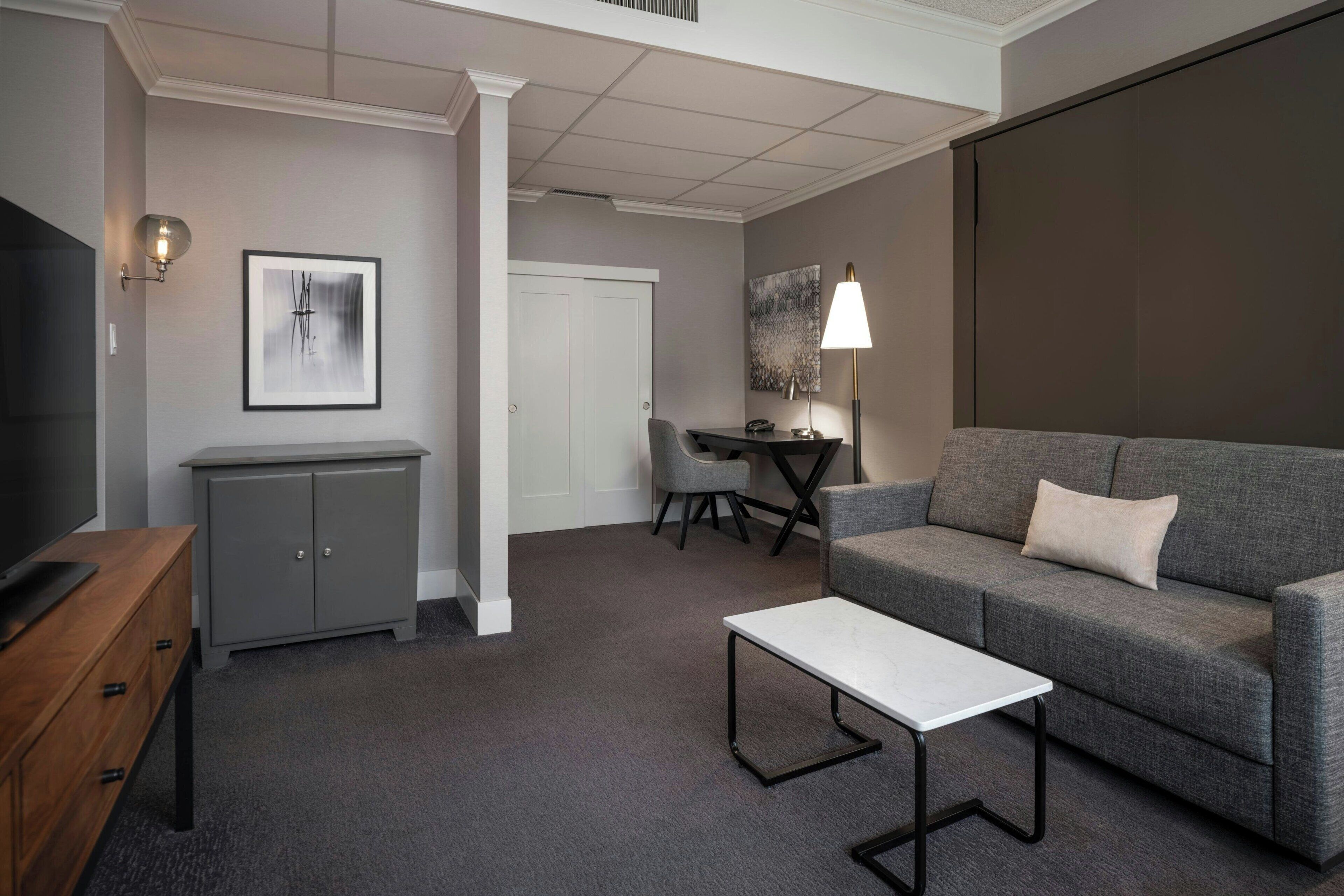 A modern living room with a grey sofa, a white coffee table, a grey cabinet, a television, and a framed abstract painting on the wall.