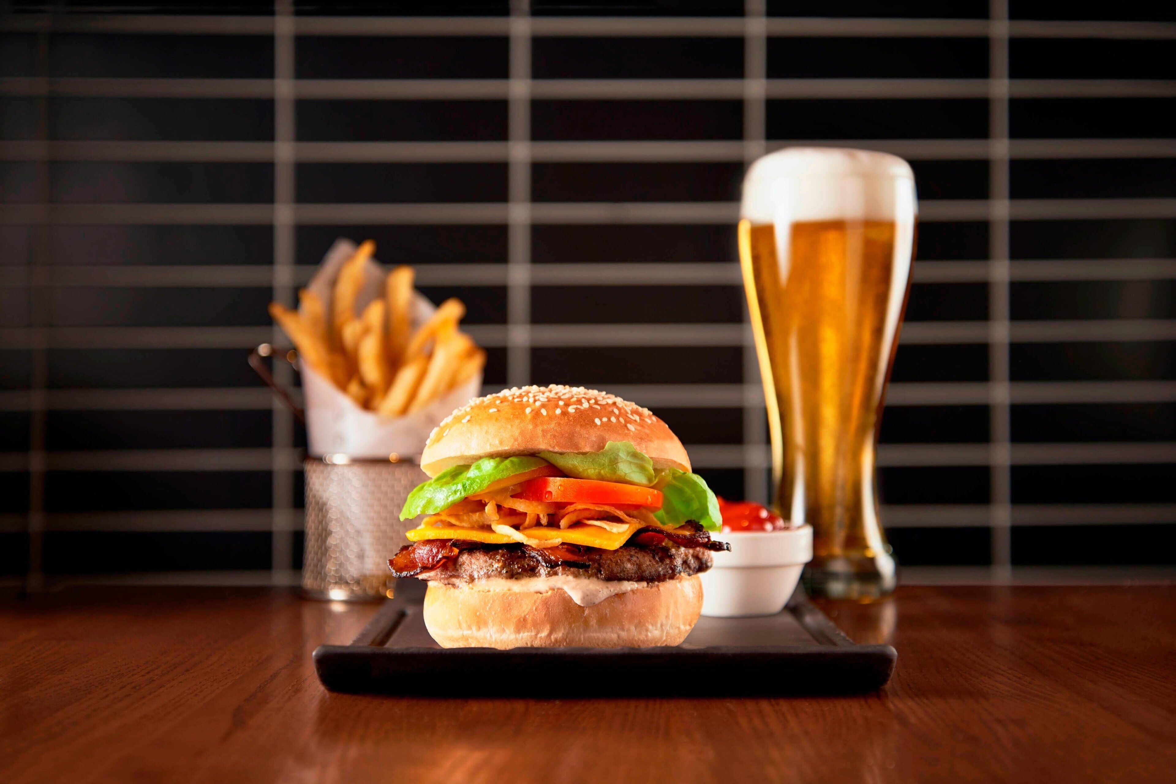 A burger with fries and a glass of beer on a wooden table.