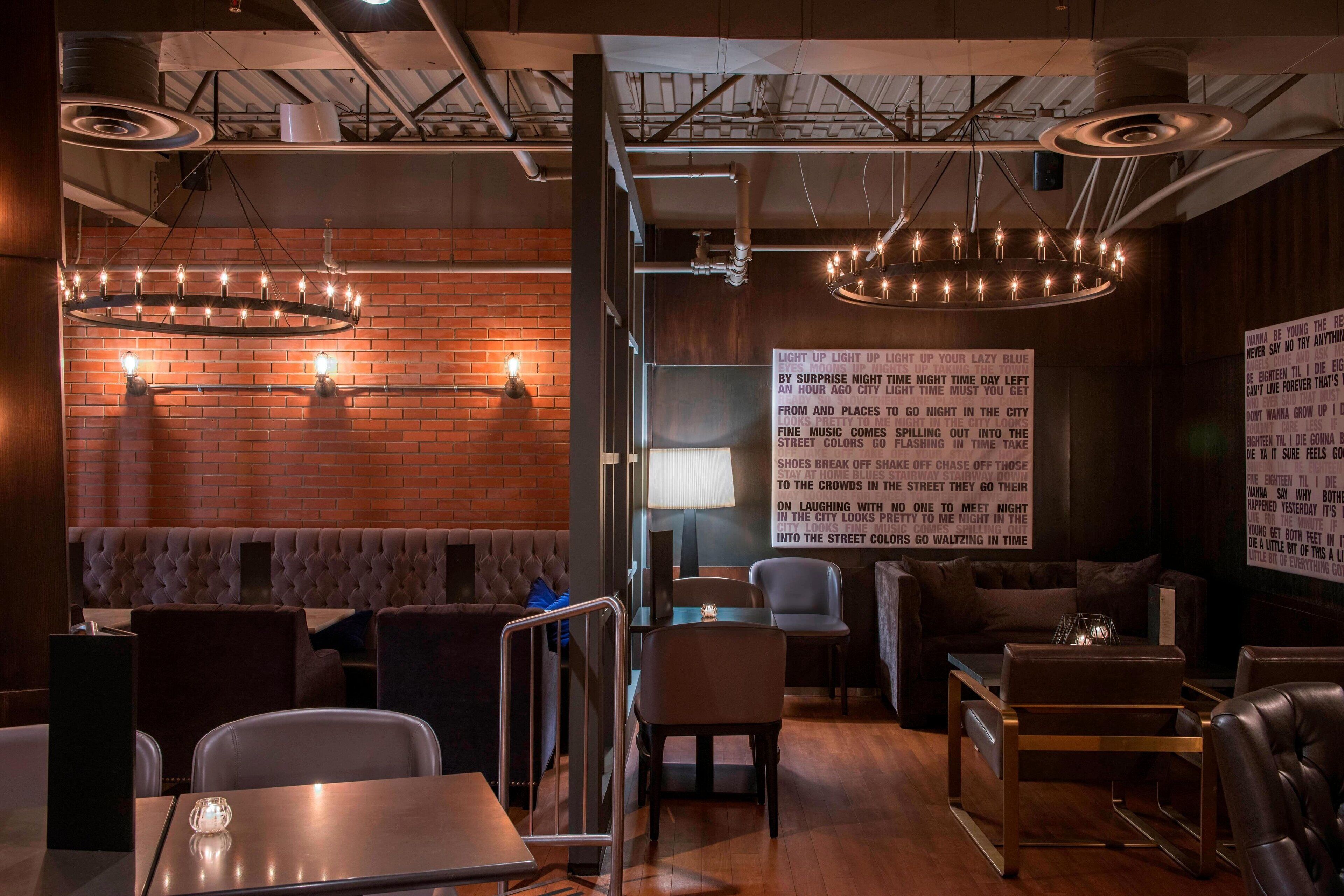 Un interior de restaurante moderno con paredes de ladrillo, tuberías del techo expuestas y una variedad de opciones de asientos, incluyendo cabinas y mesas.