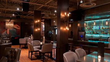 A bar area with wooden flooring, bar stools, and a bar counter with a variety of bottles.