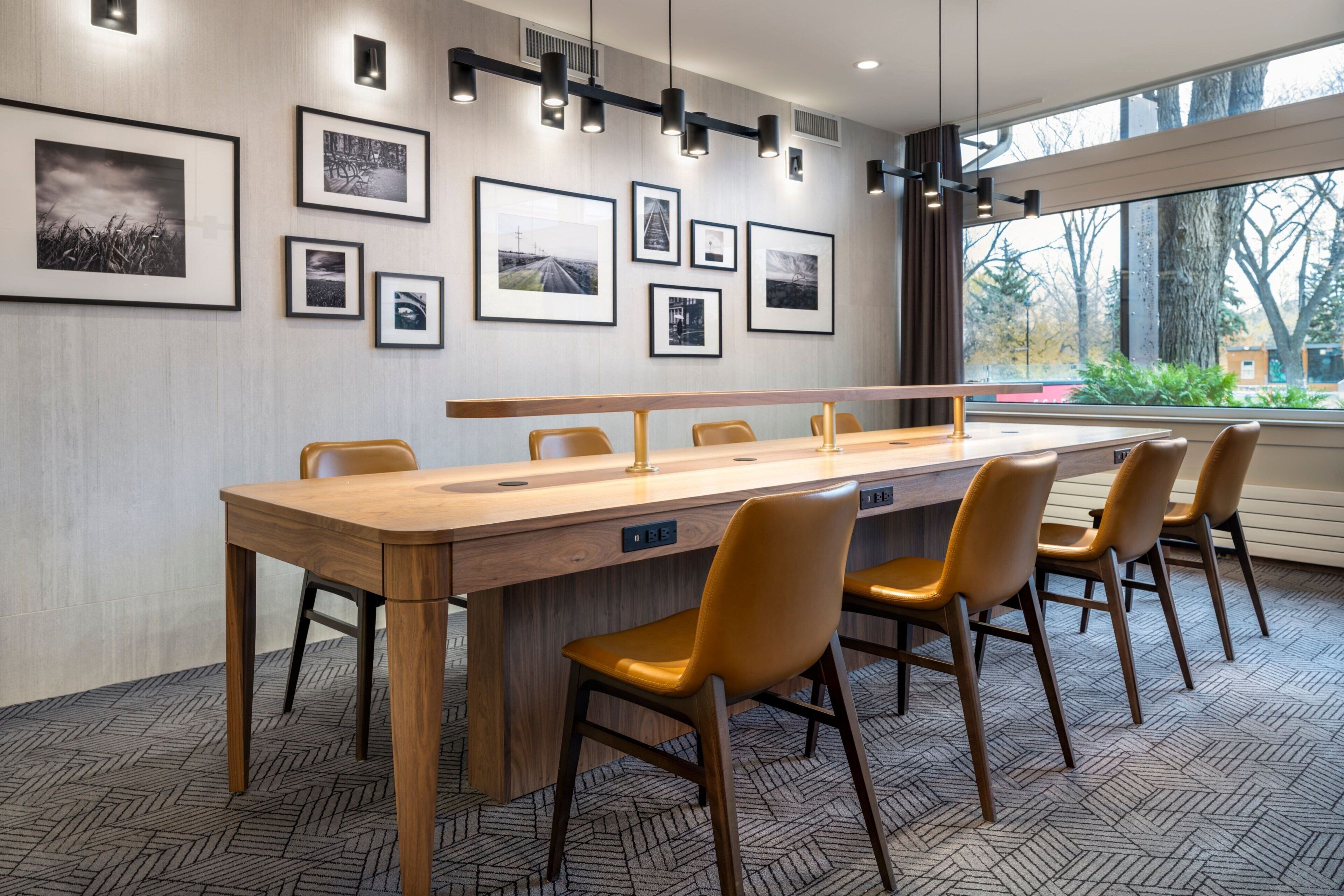 Une salle de conférence avec une longue table en bois, six chaises et des tableaux encadrés accrochés au mur.