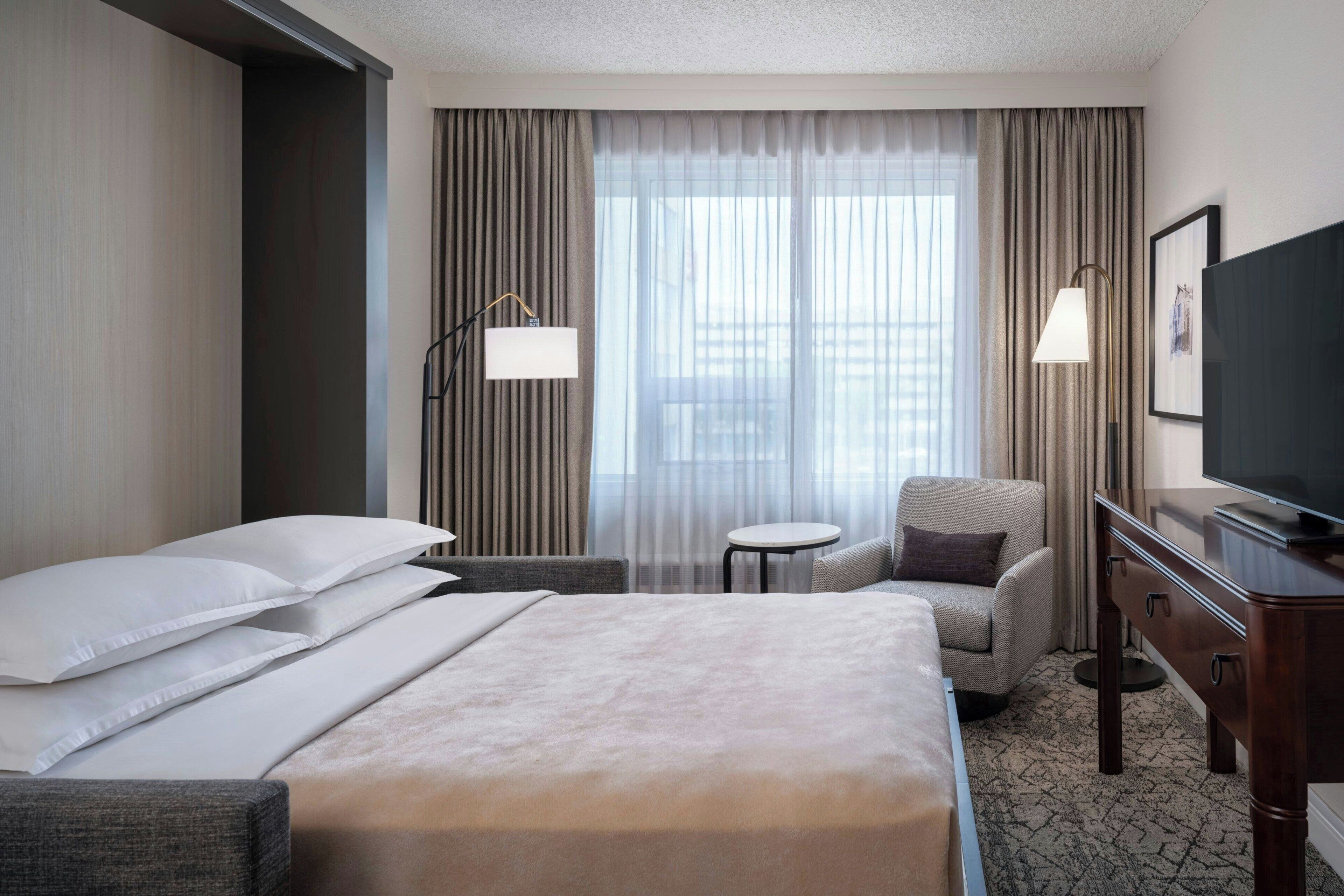 A hotel room with a large bed, a chair, a desk, and a television.