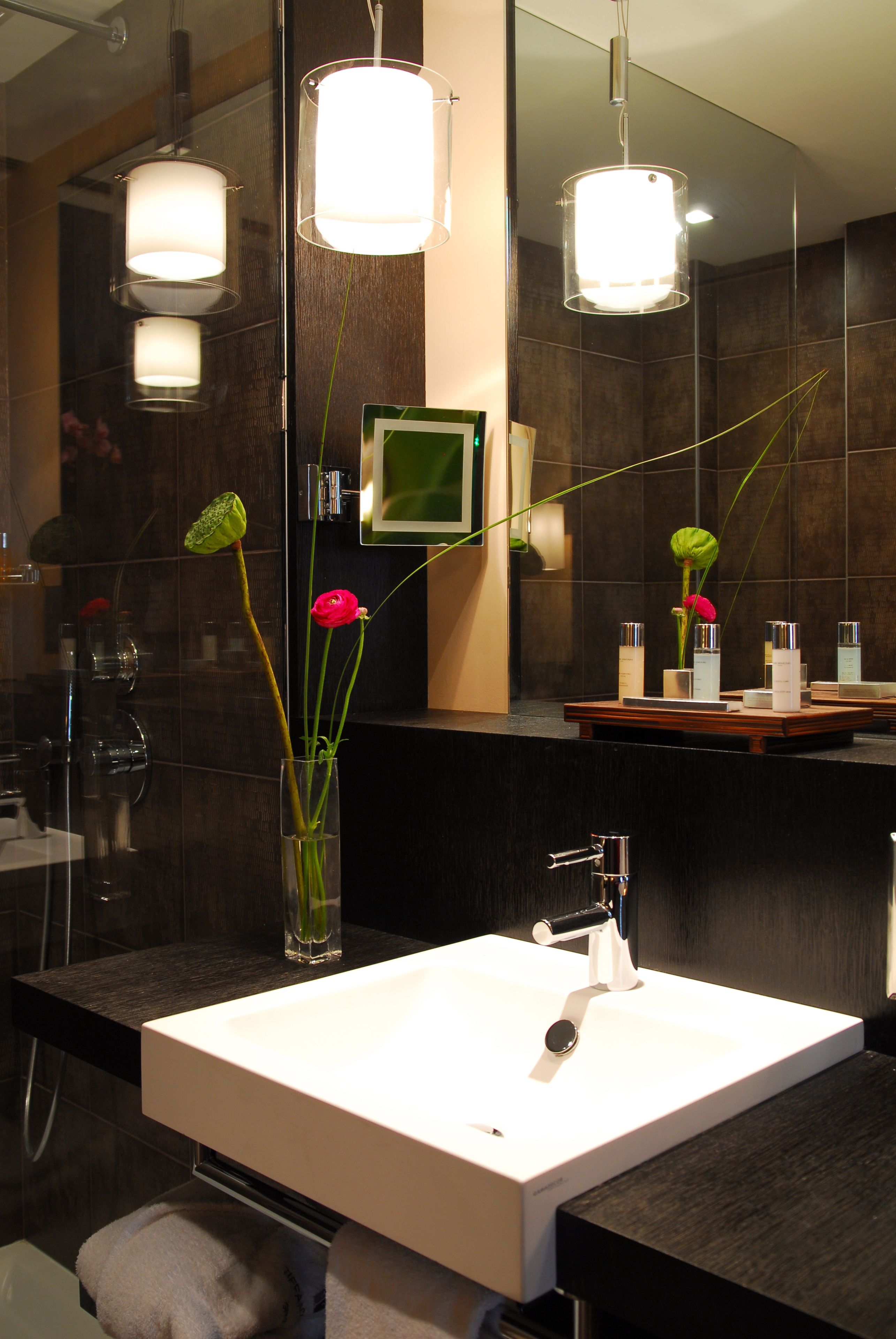 Un baño moderno con lavamanos blanco, baldosas oscuras y dos lámparas colgantes.
