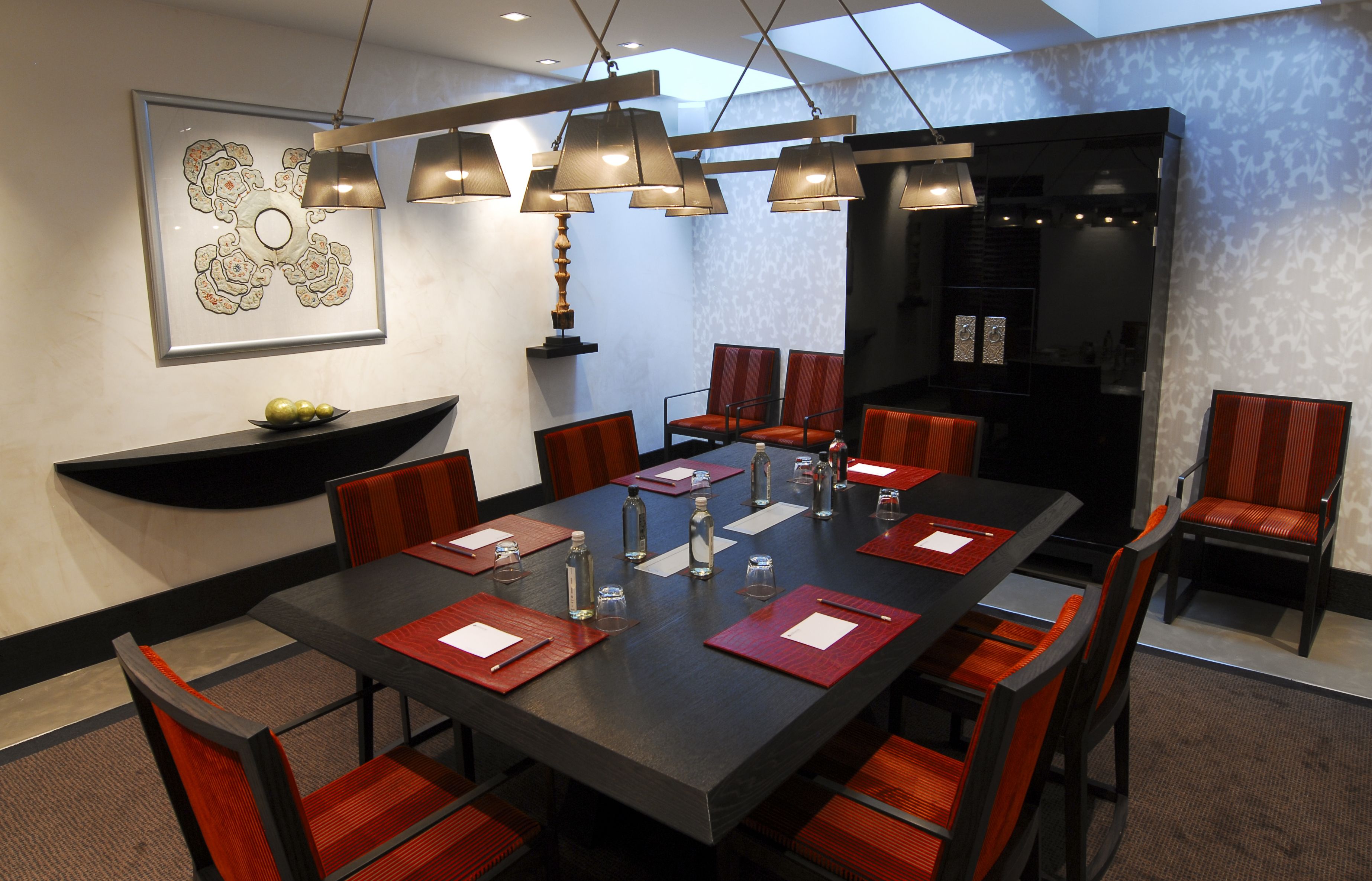 A conference room with a large table, red chairs, and a chandelier.