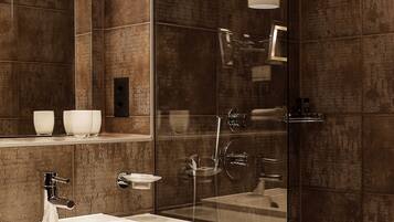 A modern bathroom with a large mirror, a white sink, a glass-enclosed shower, and pendant lighting.