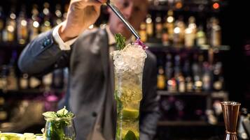 Ein Barkeeper bereitet einen Cocktail zu, mit einem hohen Glas, gefüllt mit Eis, garniert mit Minze und einer Blüte.