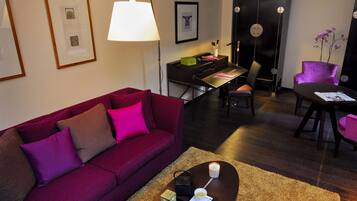 A modern living room with a purple sofa, a coffee table with a candle, and a desk area with a computer and books.