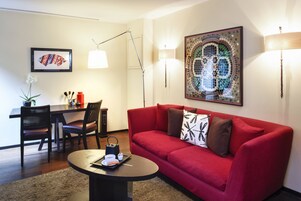 A living room with a red sofa, a coffee table, a dining area with chairs, and a wall with a mosaic artwork.