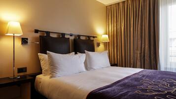 Een hotelkamer met een groot bed, twee bedlampen, een hoofdeinde en een raam met gordijnen.