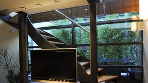 Un interior moderno con una escalera, un televisor de pantalla plana sobre un soporte de madera y vistas a la vegetación a través de grandes ventanales.