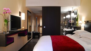 Habitación de hotel con cama, televisión, escritorio con computadora, espejo y baño.