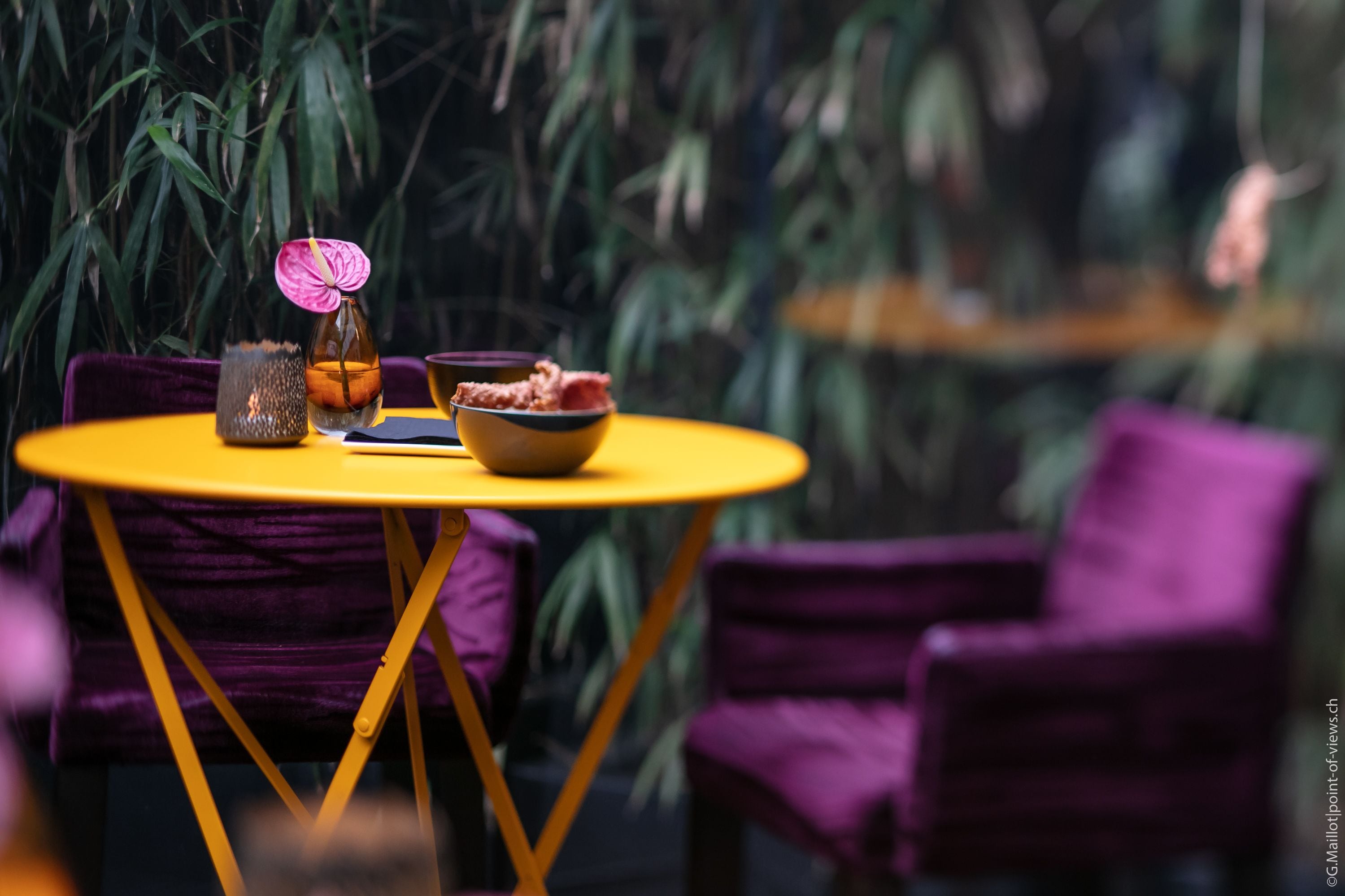 A round yellow table with a purple chair, a vase with a pink flower, and a bowl of food.