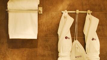A bathroom with a towel rack holding a folded towel and two white robes with a logo.