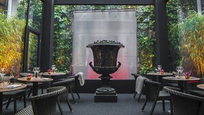 Un restaurante con mesas redondas, sillas de mimbre y una urna decorativa en el centro.