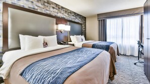 A hotel room with two beds, a large headboard, a nightstand, a lamp, and a view of the city through the window. - Comfort Hotel Airport North (Toronto)