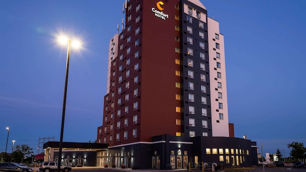 A multi-story hotel with a prominent Comfort Hotel sign, a parking lot, and a street lamp. - Comfort Hotel Airport North (Toronto)