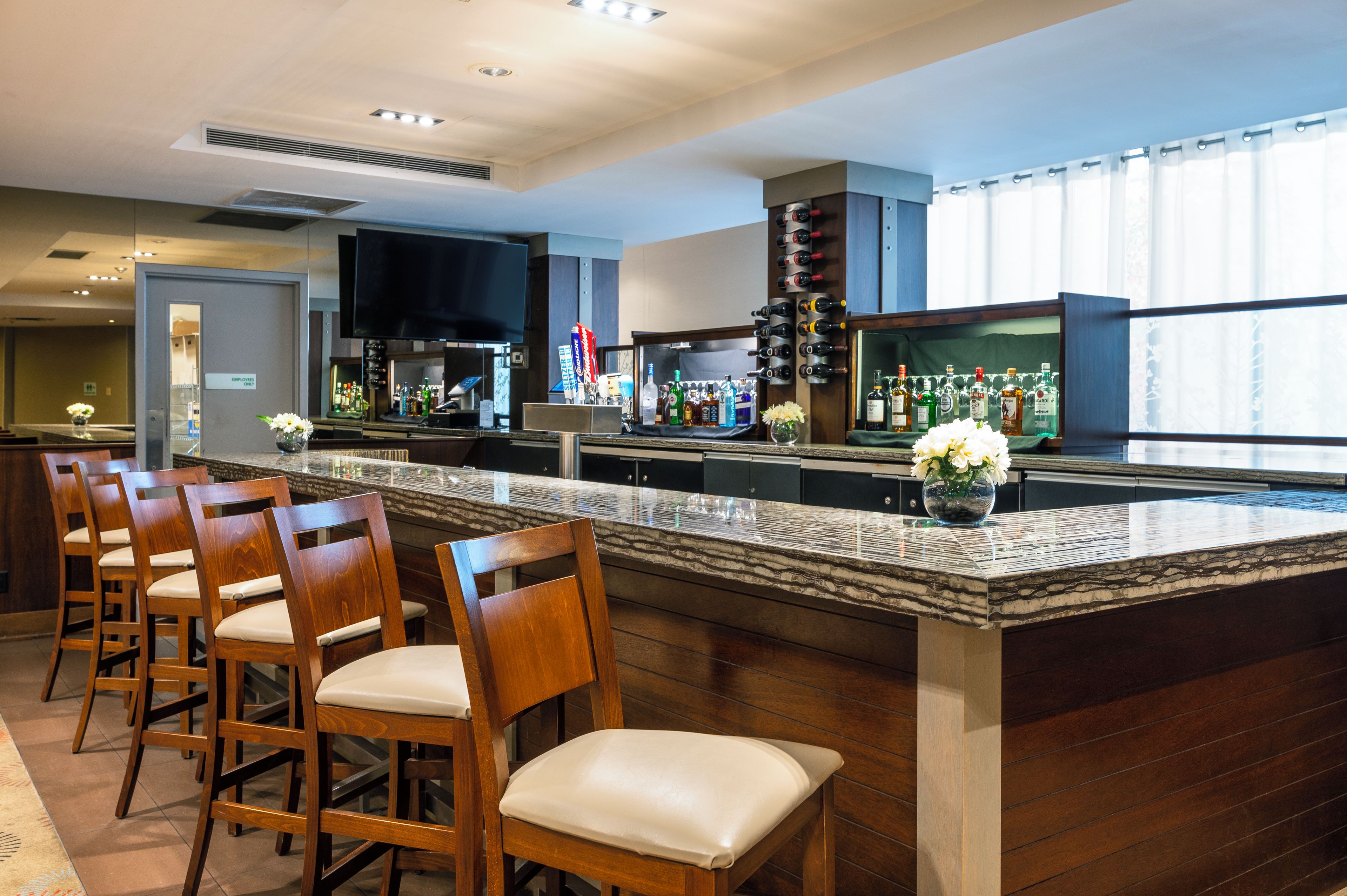 Zona de bar con sillas de madera, una barra con botellas y un televisor.