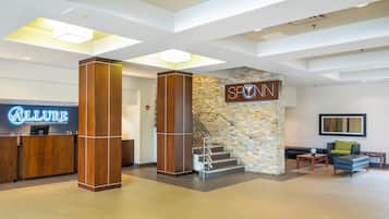 A hotel lobby with a reception desk, a staircase, and a seating area.