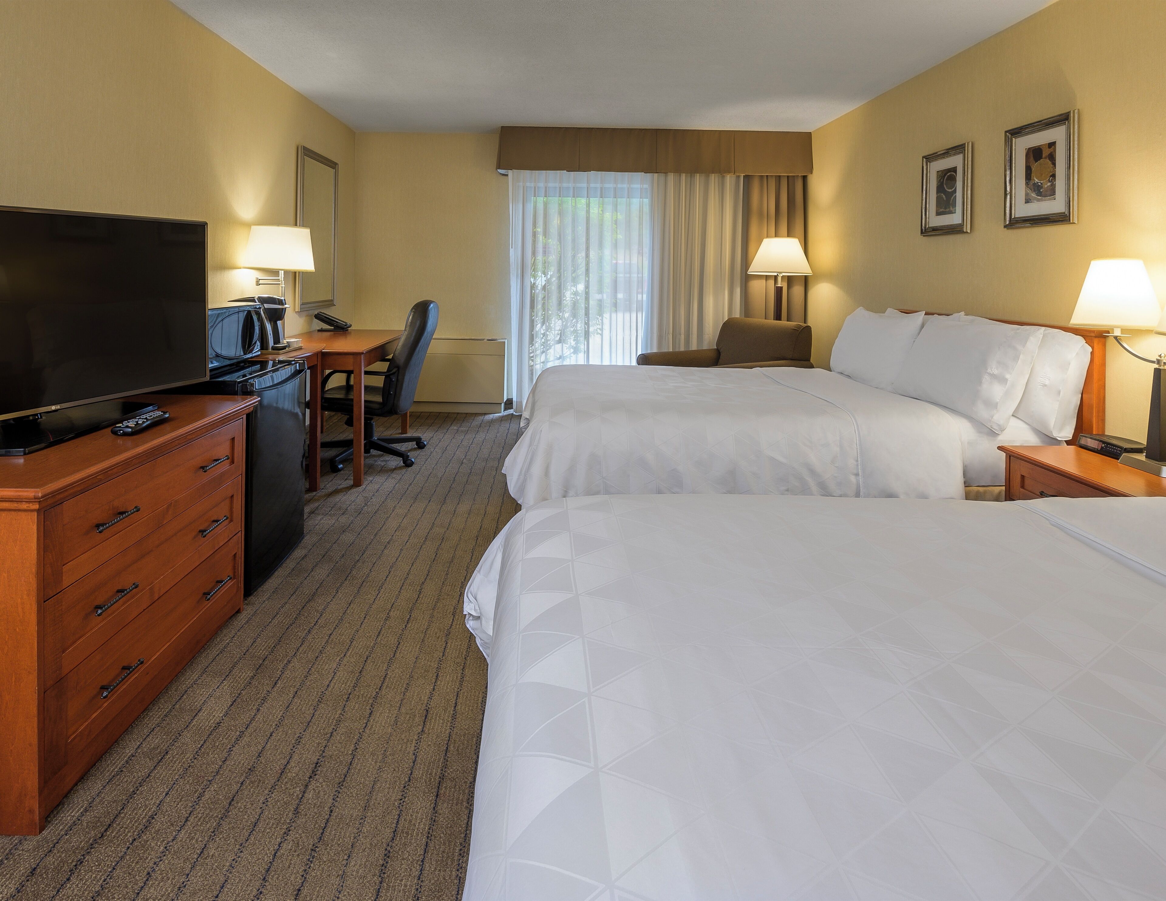 A hotel room with two beds, a desk with a TV, a chair, and two lamps.