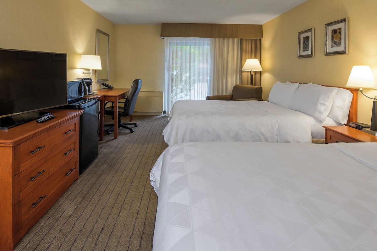 A hotel room with two beds, a desk with a TV, a chair, and two lamps.