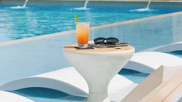A poolside setting with a drink in a glass, sunglasses, and a book on a white pedestal.