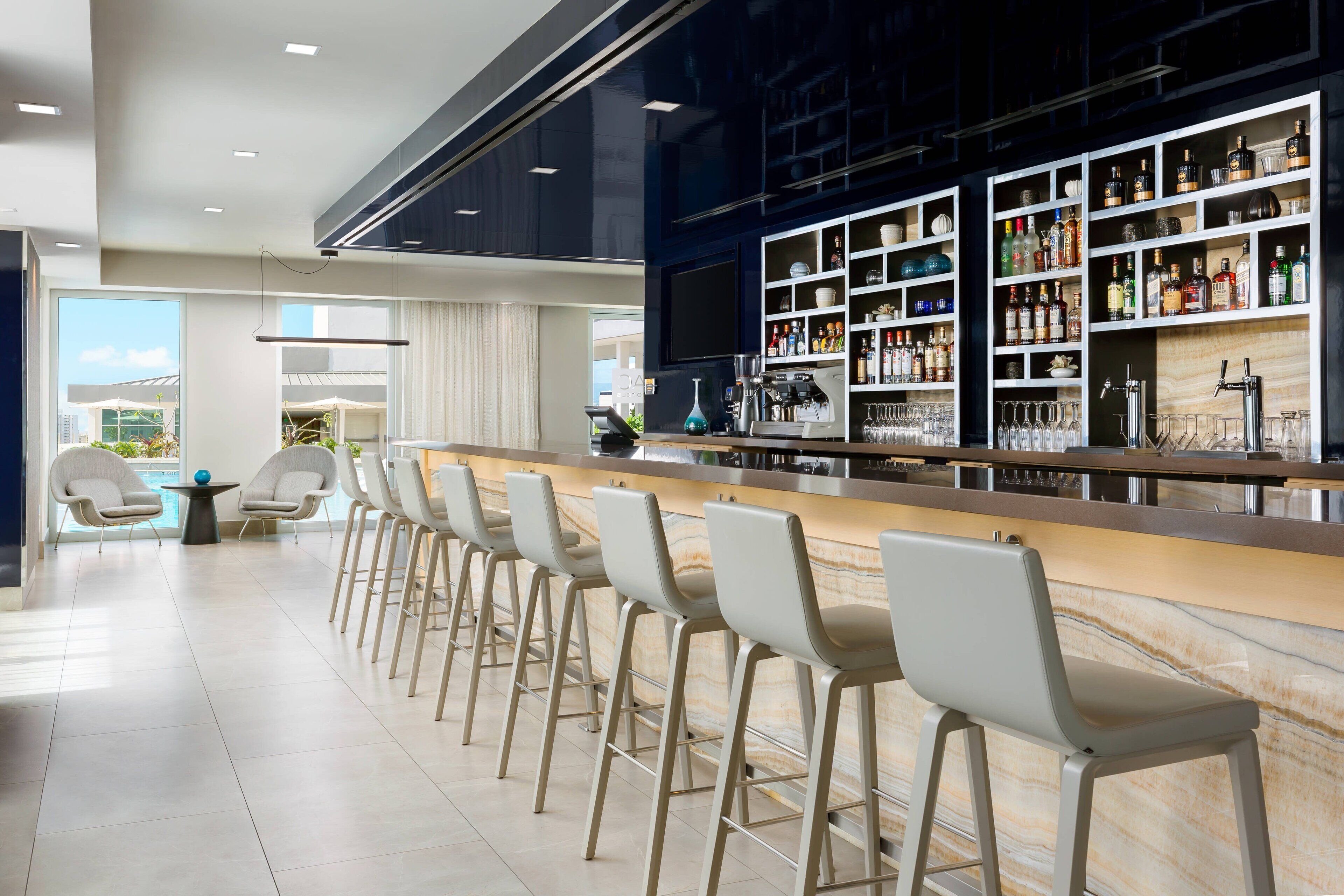 Zona de bar moderna con mostrador de mármol, taburetes y una vinoteca con botellas.