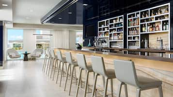 Zona de bar moderna con mostrador de mármol, taburetes y una vinoteca con botellas.